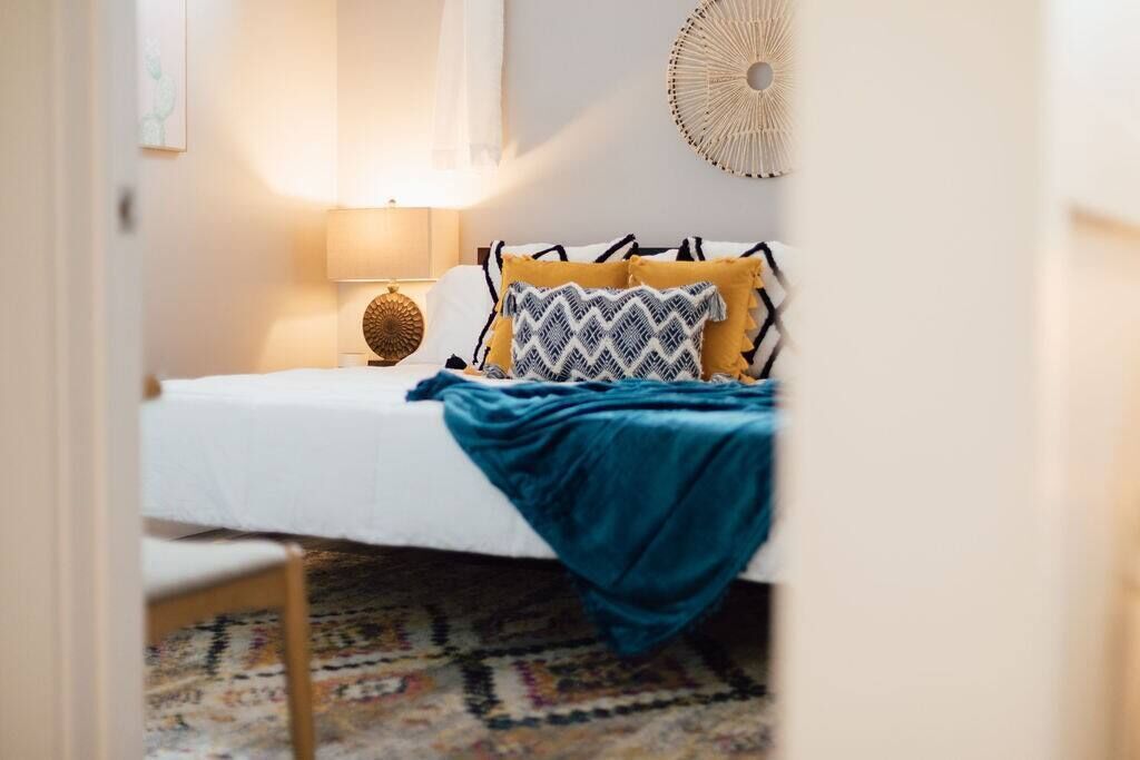 A neatly made bed with a white comforter and a blue throw blanket, a patterned rug, and a wall-mounted decorative item.