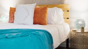 A neatly made bed with a wooden headboard, white and orange pillows, and a teal throw blanket. - Pet-Friendly Loft Downtown Near Dining & Parks 203 (Johnson City)