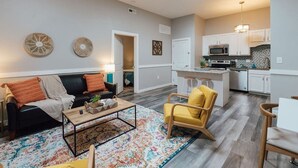 A modern living room with a black leather sofa, a yellow armchair, and a coffee table. A kitchen with white cabinets and a microwave is visible in the background. - Pet-Friendly Loft Downtown Near Dining & Parks 203 (Johnson City)