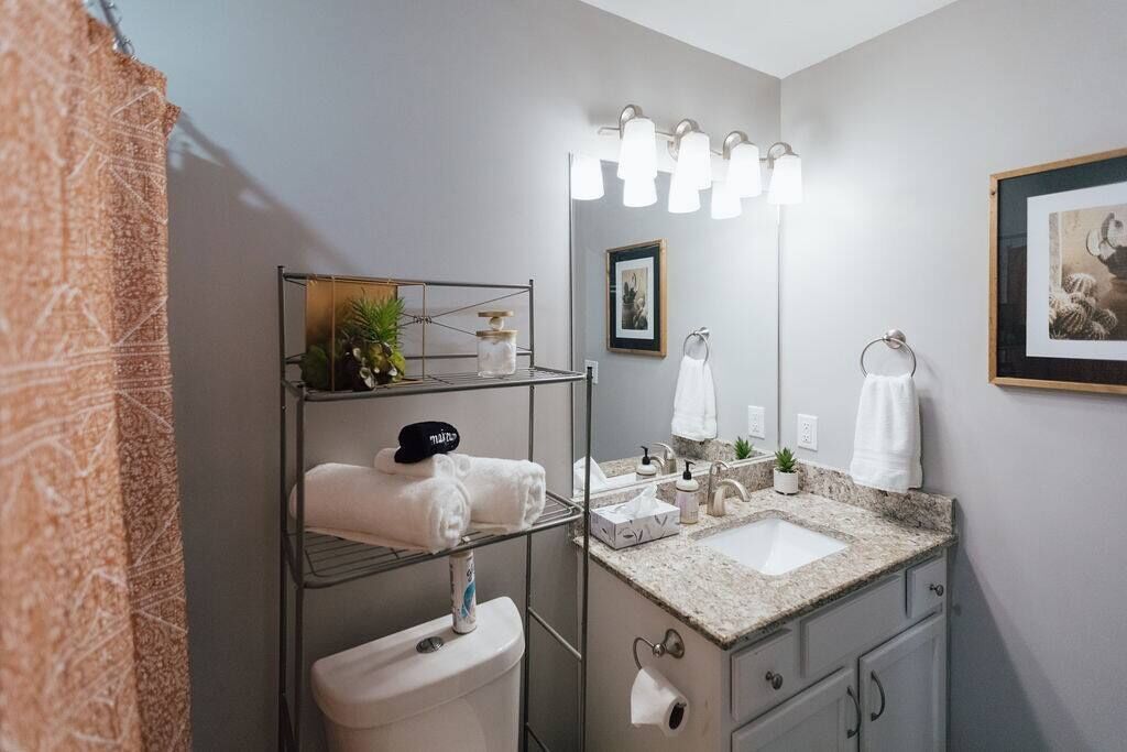 Een moderne badkamer met een wastafel met een granieten blad, een grote spiegel met verlichting, een handdoekhouder en een toilet.