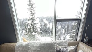 A room with a large window overlooking a snowy landscape, a beige sofa with patterned cushions, and a white knitted throw. - 3 Bed/2 Bath Home w/amazing views, BBQ, laundry, close to village & trails (Star Mountain)