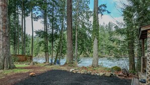 A forested area with a river, a wooden deck, and a small cabin.
