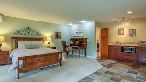 A bedroom with a wooden bed, a desk, a chair, and a kitchenette.