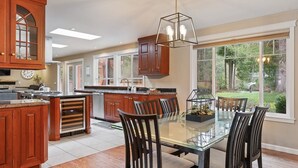Une cuisine spacieuse dotée de meubles en bois, d’un grand îlot central et d’un coin repas avec une table et des chaises en verre.