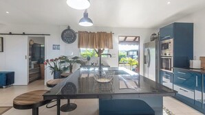 A modern kitchen with a central island, blue cabinets, and a large window. - Villa Priva • Meilly Estate (Saint-Louis)