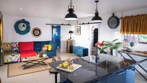 A modern kitchen with a central island, a dining area with a blue sofa, and a living room with a colorful sofa. - Villa Priva • Meilly Estate (Saint-Louis)