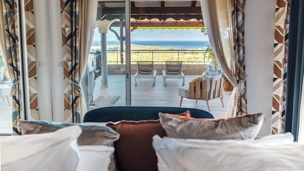 A bedroom with a bed, pillows, and a view of the beach through a glass door. - Villa Priva • Meilly Estate (Saint-Louis)