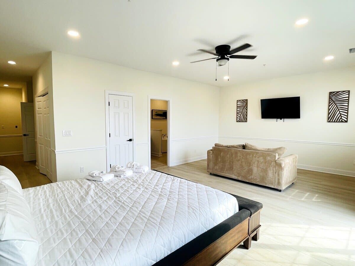 A bedroom with a large bed, a ceiling fan, a sofa, and a TV on the wall.