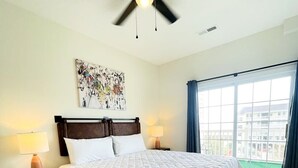 Une chambre d’hôtel avec un lit, deux tables de chevet avec des lampes, un ventilateur de plafond, une fenêtre avec des rideaux et une vue sur la ville.