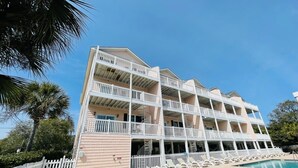 Un hôtel à plusieurs étages, doté de balcons, d’une piscine et d’une clôture blanche.