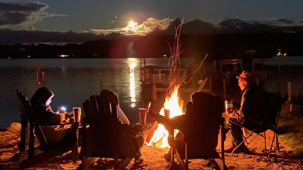 Eine Gruppe von Menschen sitzt nachts an einem Lagerfeuer am Seeufer.