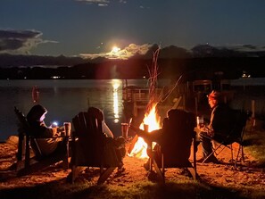 Eine Gruppe von Menschen sitzt nachts an einem Lagerfeuer am Seeufer.