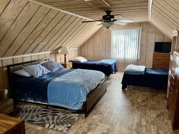 Ein Schlafzimmer mit zwei Betten, einem Deckenventilator, einem Fenster mit Jalousien und einer Holzkommode.