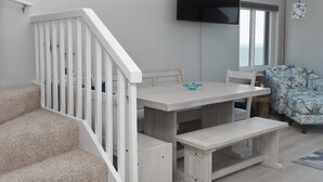 Une pièce avec un escalier blanc, une table en bois avec des bancs, un téléviseur à écran plat fixé au mur et une fenêtre donnant sur la mer.
