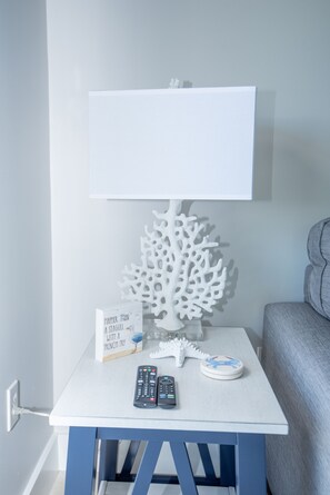 Uma mesa branca com uma escultura de coral branco, uma placa, dois controles remotos e um prato decorativo.