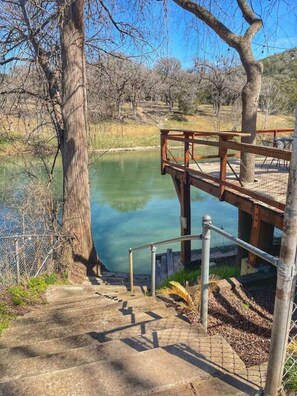 A wooden staircase leading to a viewing platform over a calm lake, surrounded by trees and a fenced area.