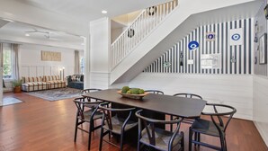 Et moderne spiseområde med et træbord og stole, en trappe med en stribet væg, og udsigt til en stue med en sofa og en plante.