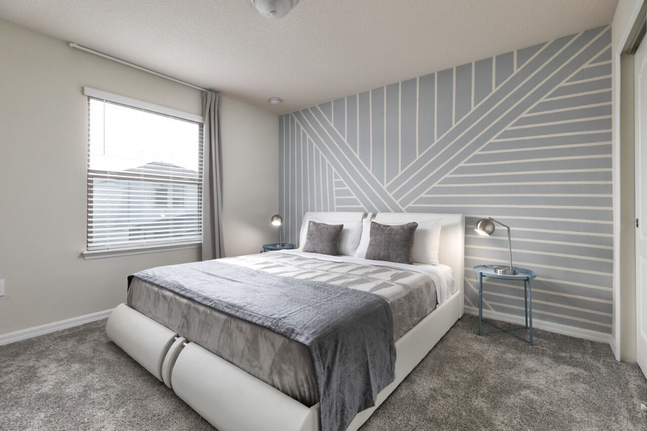 A modern bedroom with a large bed, a geometric-patterned wall, and a window with blinds.