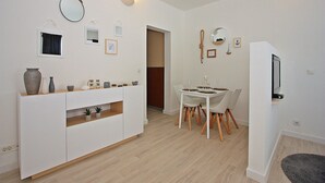 Un salon moderne et bien éclairé, comprenant un coin repas, des meubles blancs et un téléviseur fixé à un mur blanc.