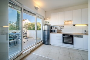 A modern kitchen with white cabinets, stainless steel appliances, and a sliding glass door leading to an outdoor patio. - Apartments Tomy - One Bedroom Apartment with Balcony and Sea view (Sutivan)