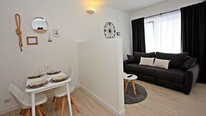 Un salon moderne comprenant un coin repas, un canapé, une horloge et un luminaire fixé au mur.