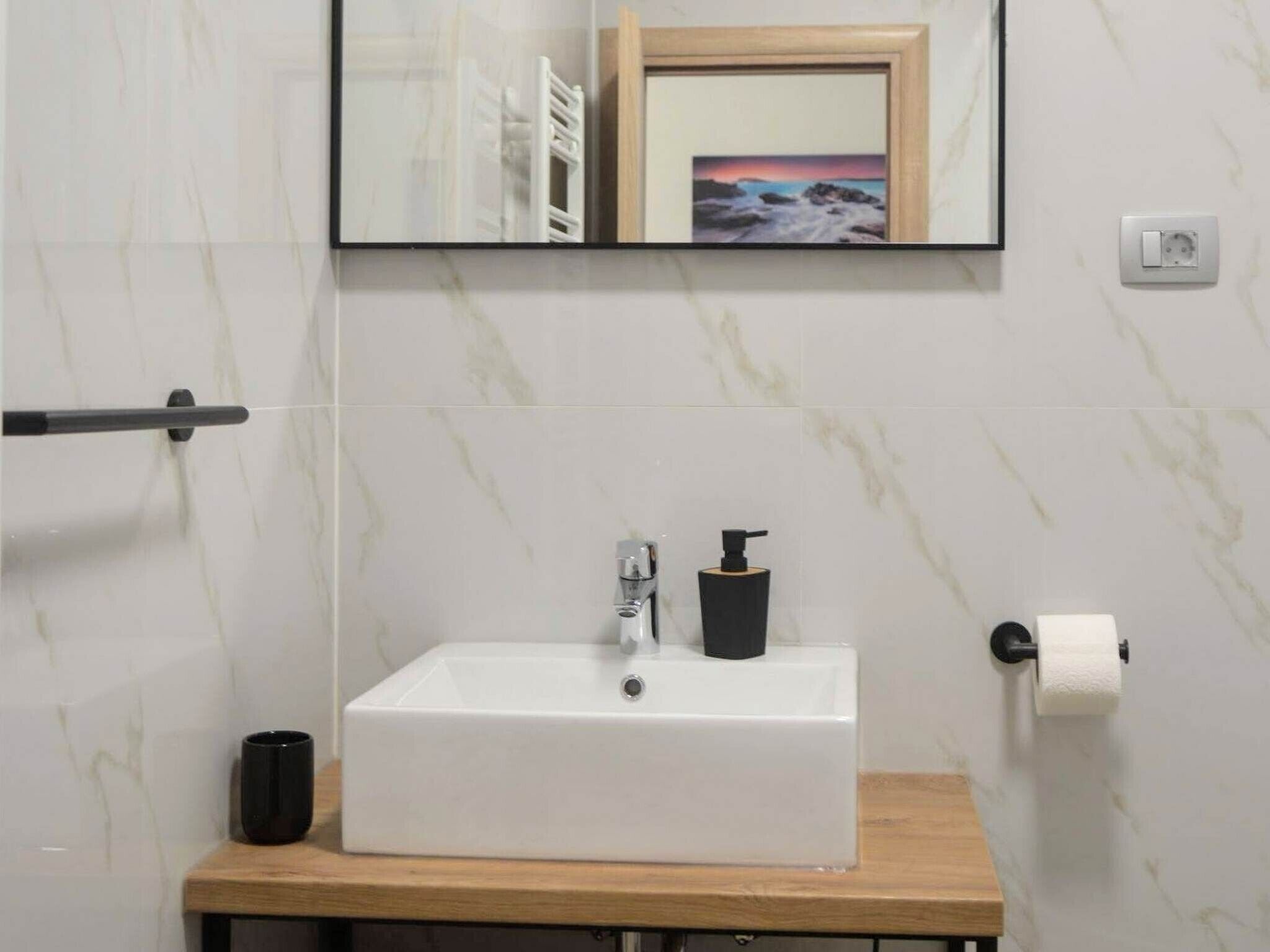A bathroom with a white sink, a mirror, a wooden countertop, and a towel rack.