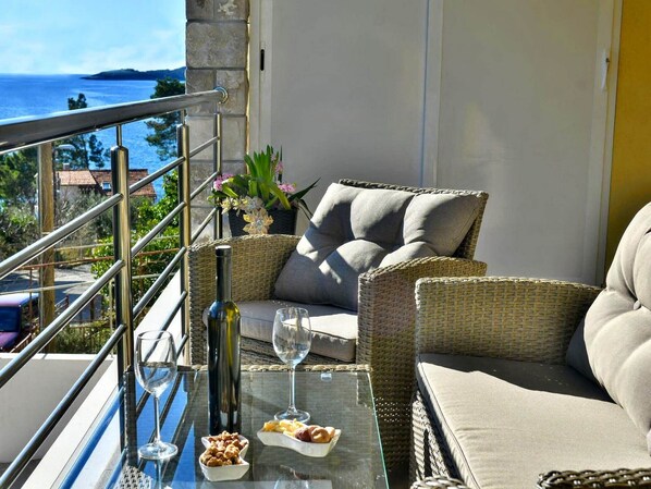 A balcony with wicker furniture, a glass table, and a view of the sea.