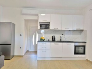 A modern kitchen with white cabinets, a stainless steel refrigerator, a microwave, a coffee maker, and an oven.