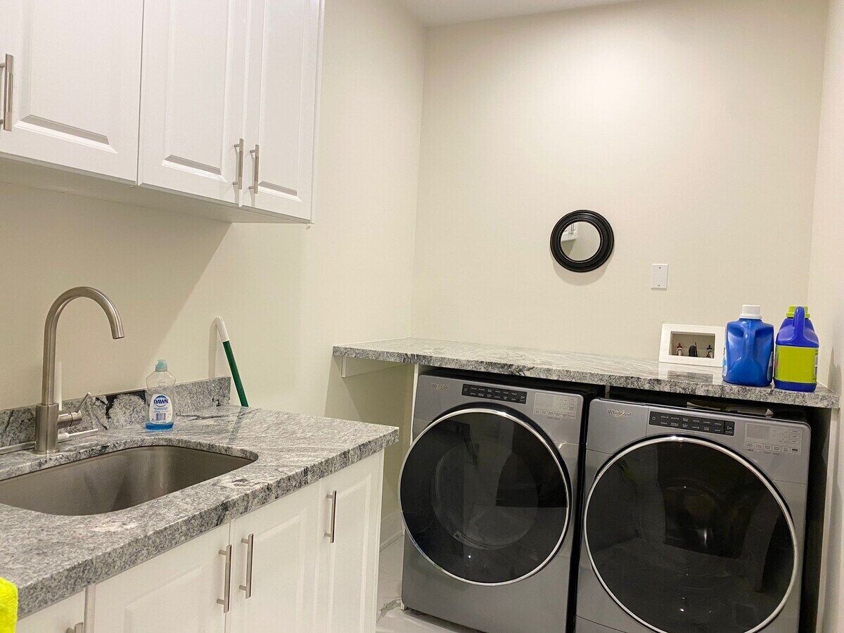 A compact kitchen with a sink, two washing machines, and a small countertop with cleaning supplies.