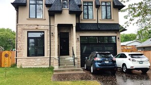 A two-story house with a stone facade, a black roof, and a garage with two cars parked inside. - Dazzling Home Next to Beach & Go Station (Pickering)