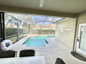 Un patio techado con piscina, mobiliario exterior y vista a una zona residencial.