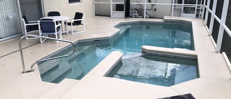 An indoor swimming pool with a tiled deck, a few lounge chairs, and a covered area with a table and chairs.