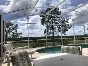 A covered outdoor area with a pool, lounge chairs, and a view of a golf course. - 5 Bedroom, Pool Home Overlooking Golf Course. Close to Attractions (Davenport)