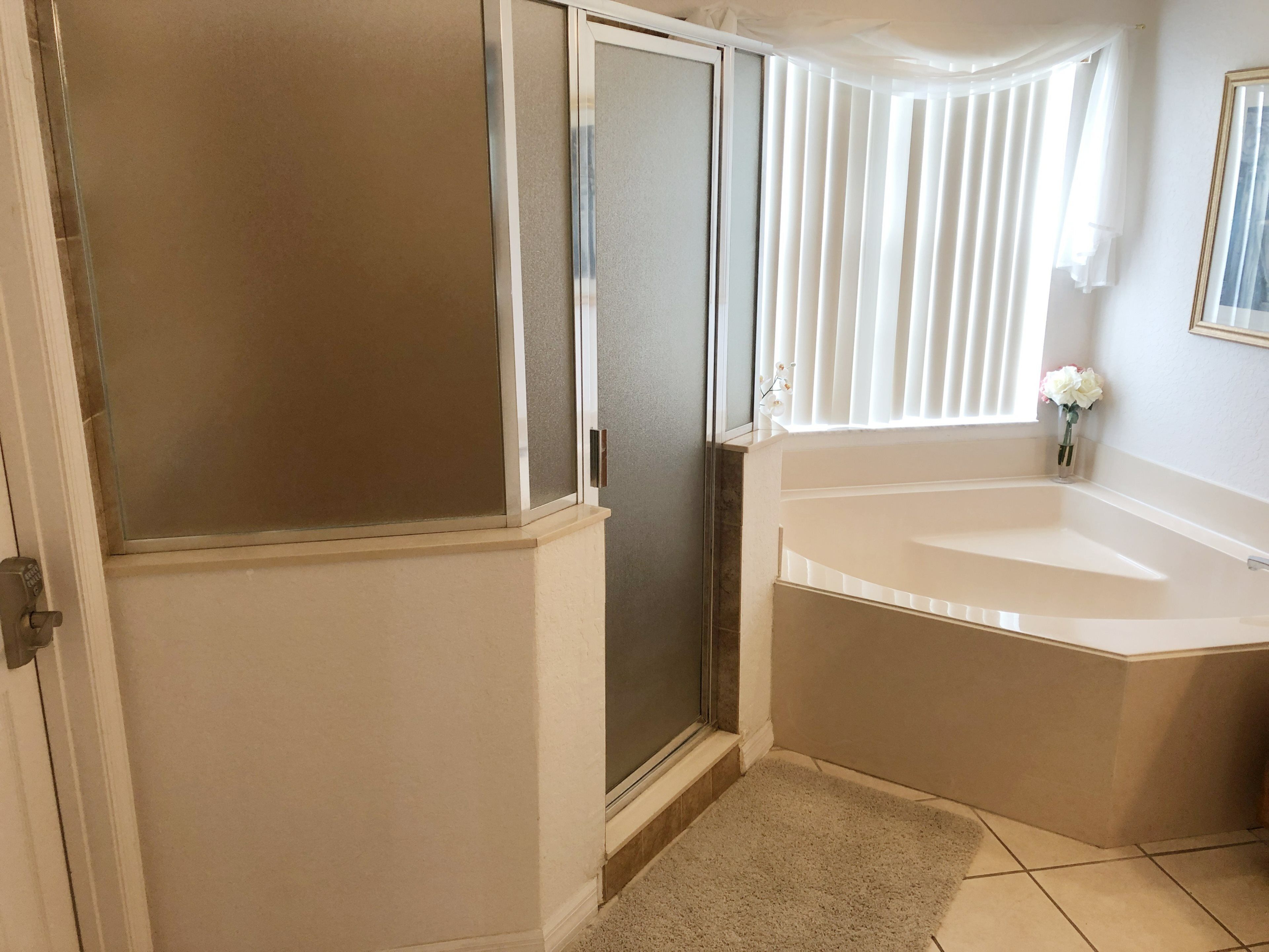 A bathroom with a shower, a sink, and a window with blinds.