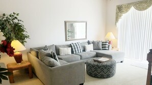 A living room with a grey sectional sofa, a round ottoman, a potted plant, and a framed artwork on the wall. - 5 Bedroom, Pool Home Overlooking Golf Course. Close to Attractions (Davenport)