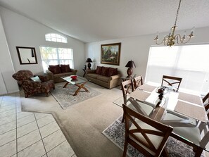 A living room with a dining area, two sofas, a coffee table, and a chandelier. - 4 bedroom  single story house with south facing pool and spa close to Disney (Kissimmee)