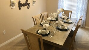 Ein Esszimmer mit einem langen Tisch, gedeckt für sechs Personen, umgeben von Holzstühlen.