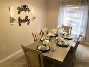Ein Esszimmer mit einem langen Tisch, gedeckt für sechs Personen, umgeben von Holzstühlen.