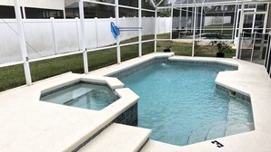 Ein Schwimmbecken mit Whirlpool, umgeben von einem weißen Zaun und einer Gewächshauskonstruktion.
