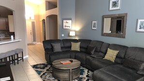 Ein modernes Wohnzimmer mit einem dunkelgrauen Ecksofa, einem runden Couchtisch und einem gemusterten Teppich.