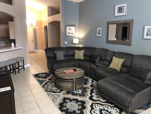 Ein modernes Wohnzimmer mit einem dunkelgrauen Ecksofa, einem runden Couchtisch und einem gemusterten Teppich.