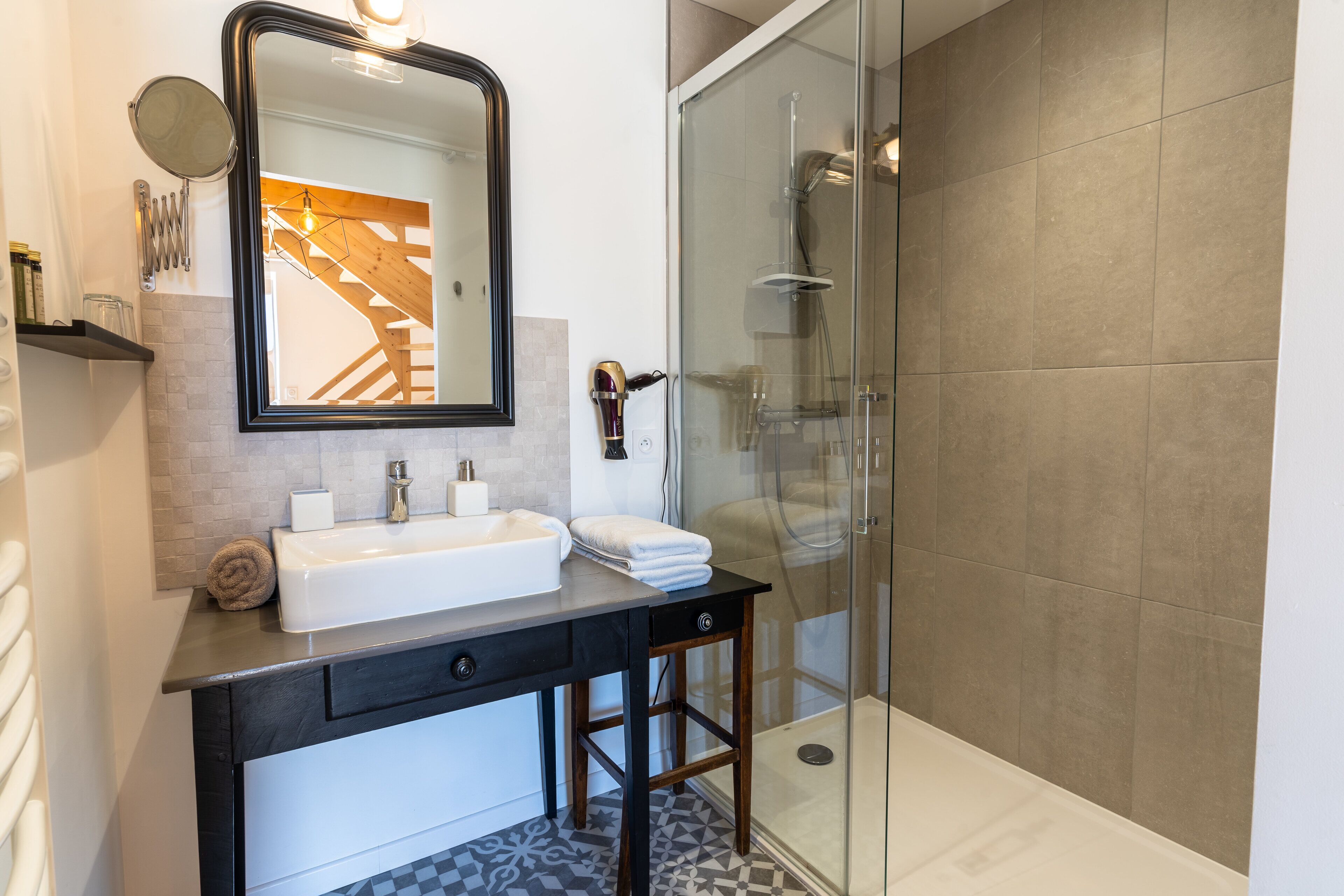 A modern bathroom with a white sink, dark countertop, and a glass shower enclosure.