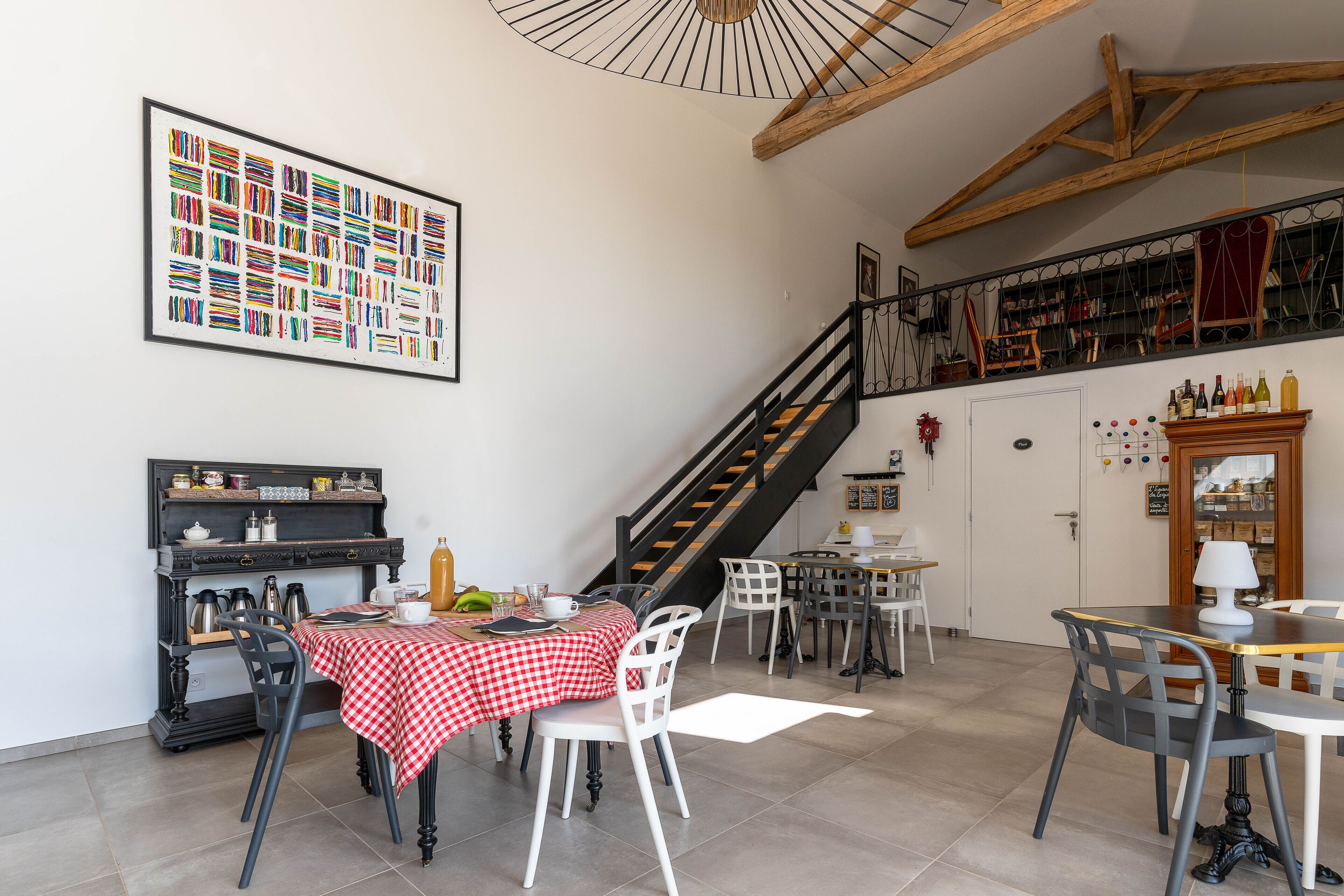 Een eetgedeelte met een trap, een boekenkast en een groot gepresenteerd schilderij aan de muur.