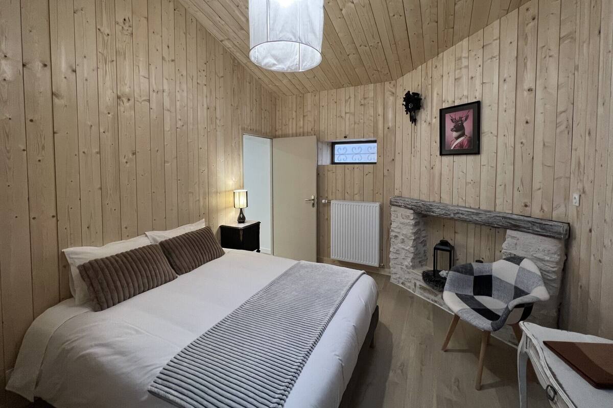 Ein Schlafzimmer mit Holzwänden, einem Bett, einer Nachttischlampe und einem Steinkamin.