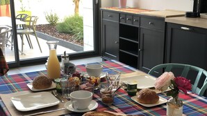 Ein Frühstückstisch mit verschiedenen Speisen, darunter Brot, Gebäck und Getränke, auf einer bunten karierten Tischdecke.