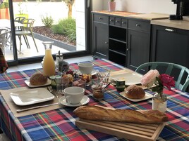 Uma mesa de café da manhã com diversos alimentos, incluindo pão, doces e bebidas, sobre uma toalha xadrez colorida.