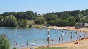 Ein Strand mit badenden und sonnenbächelnden Personen, einem Rettungsschwimmturm und Booten im Wasser.