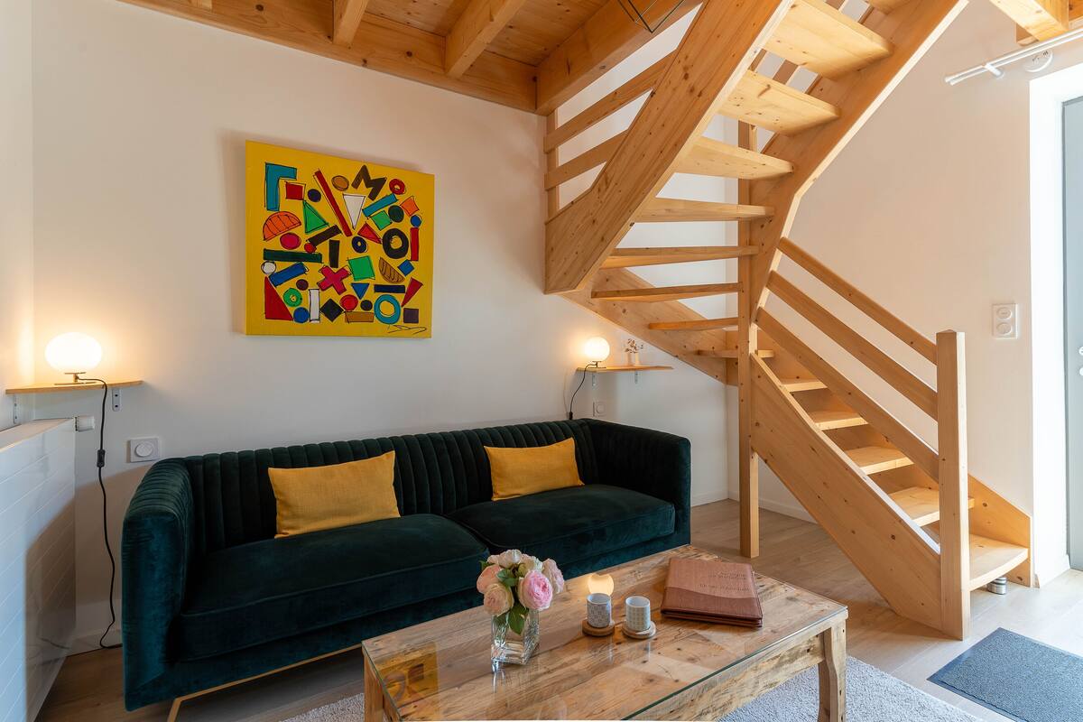 Ein modernes Wohnzimmer mit einem dunkelgrünen Sofa, einer Holztreppe und einem farbenfrohen, abstrakten Gemälde an der Wand.