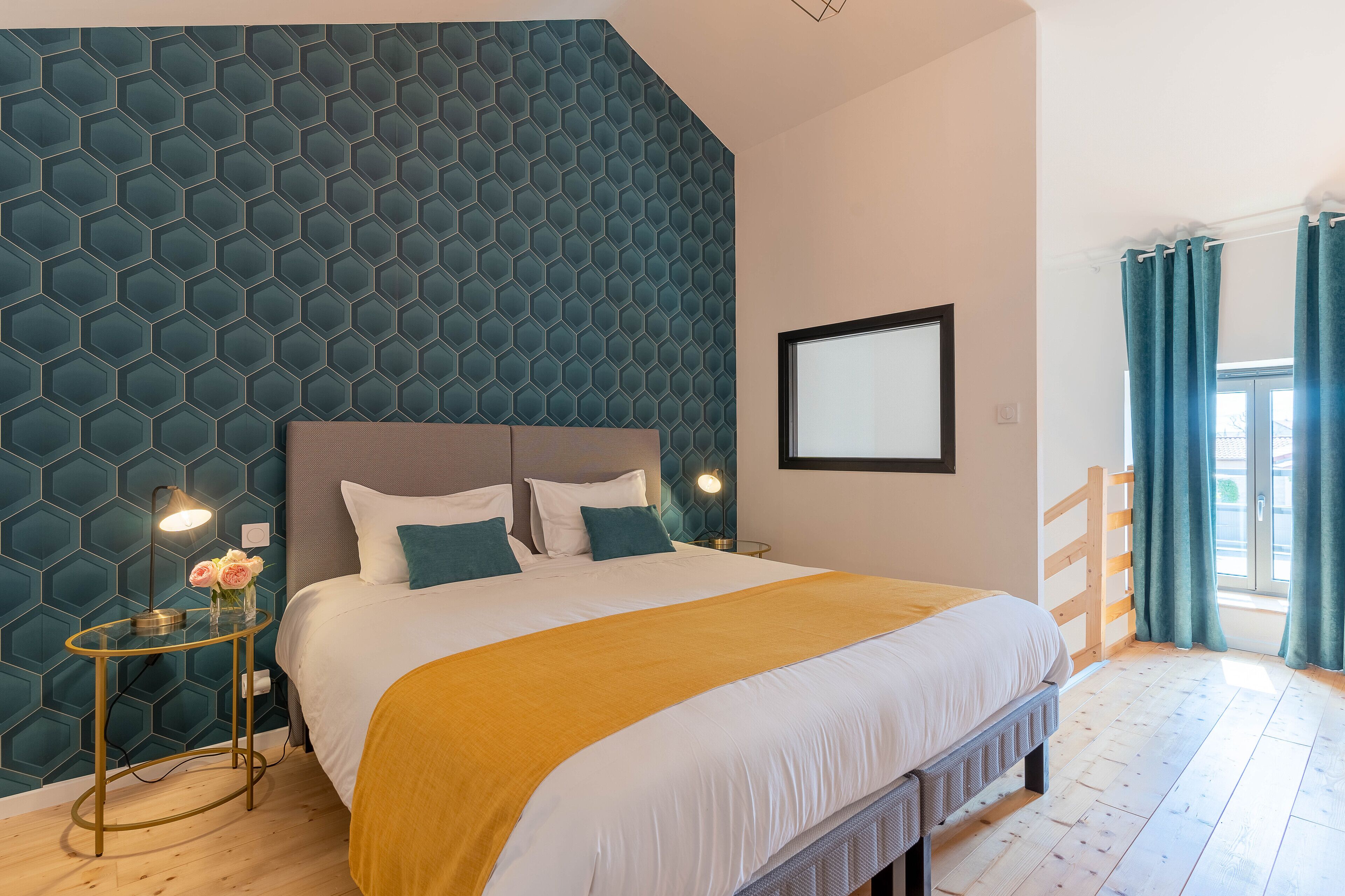 A modern bedroom with a large bed, a glass side table with a lamp, and a geometric patterned wall.