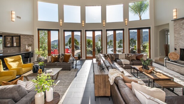 Un salon spacieux, doté d’un grand canapé, d’une table basse et d’une cheminée. De nombreuses fenêtres offrent une vue sur l’extérieur.